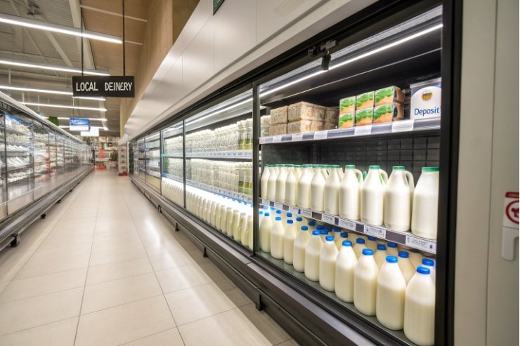 Refrigerated supermarket dairy aisle with rows of bottled milk and deposit signage