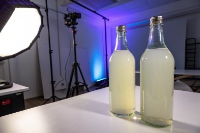 Two clear glass bottles with cloudy beverage on studio tabletop under soft lighting