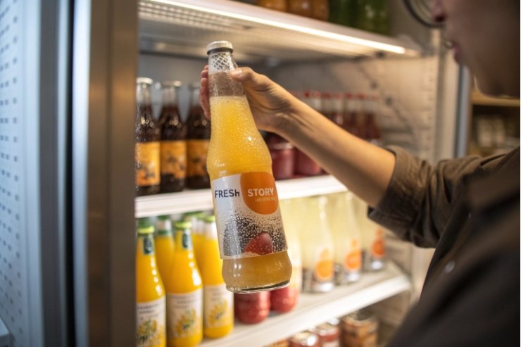 Customer holding chilled juice glass bottle from refrigerator display, condensation on label.