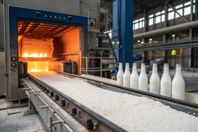 White glass bottles exiting annealing lehr on conveyor with hot furnace tunnel in factory