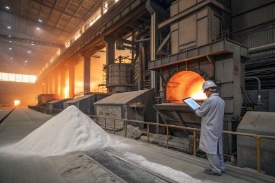 Glass plant operator monitoring furnace beside silica sand pile and molten glass production line