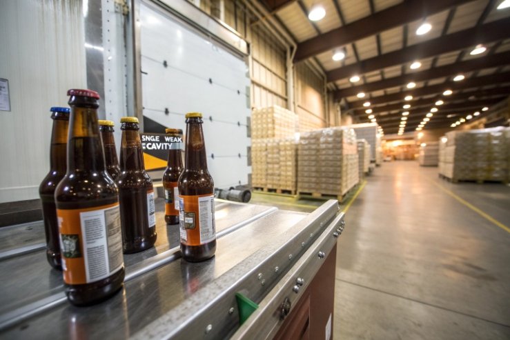 Amber beer bottles on inspection table in warehouse with palletized cartons ready for shipping.