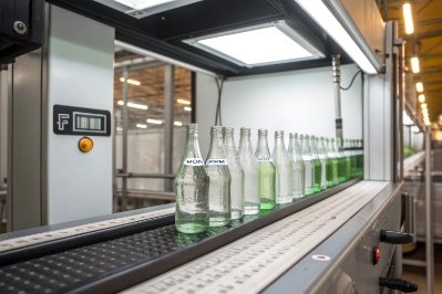 Green glass bottles on conveyor passing through automated inspection light tunnel