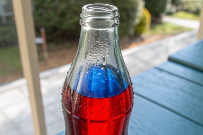 Condensation droplets on glass soda bottle with red and blue liquid layers outdoors
