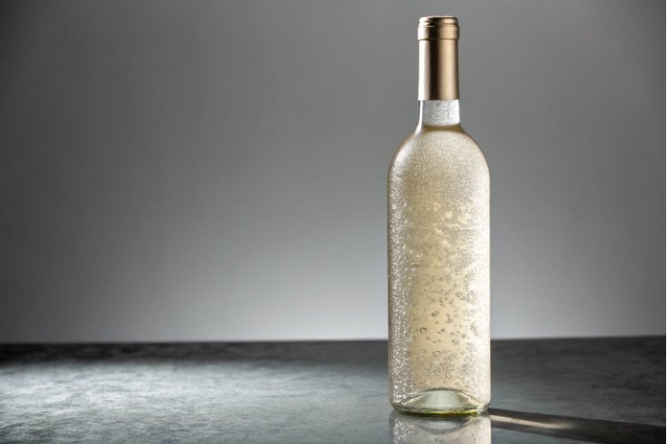 Chilled frosted white wine bottle with condensation on elegant grey studio background