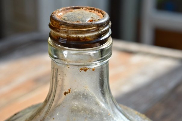 Close-up of glass bottle neck with residue buildup showing cap corrosion and contamination