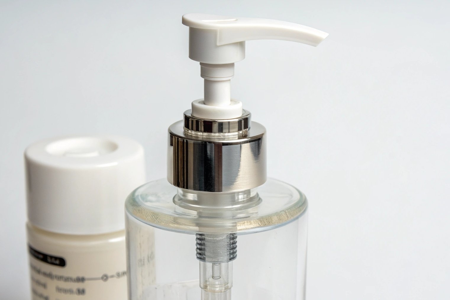 close up white lotion pump with silver collar on clear cosmetic bottle