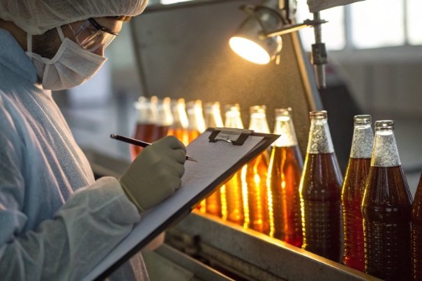 Quality inspector recording checks on amber bottles during hot filling production line