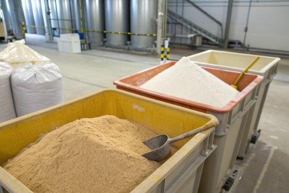 Raw glassmaking materials in large bins inside industrial glass factory warehouse