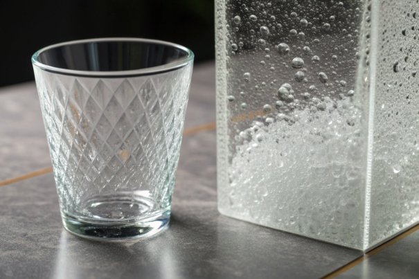 Textured drinking glass beside clear container with bubbling solution on tabletop