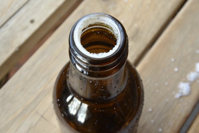 Amber glass bottle neck with white salt residue buildup around opening on wooden surface