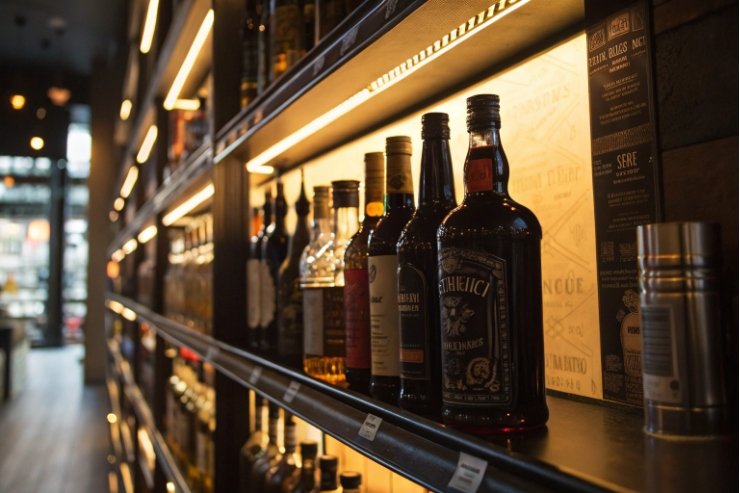 Premium whisky bottles lined on illuminated retail shelf with labels and price tags.