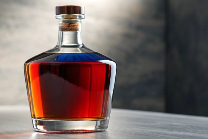 Square whisky decanter bottle with amber liquor and wood cap on table