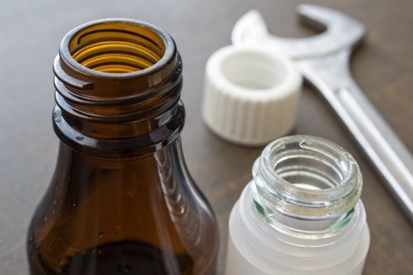 Close-up of amber bottle neck threads with white cap, wrench, and vial opening