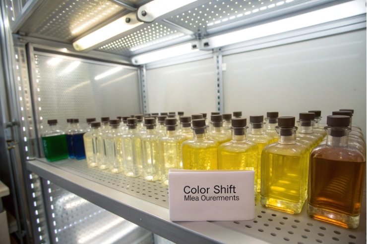 Rectangular glass perfume bottles undergoing color shift stability test on metal shelf