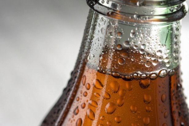 Close-up of cold amber drink bottle with condensation droplets and foam line