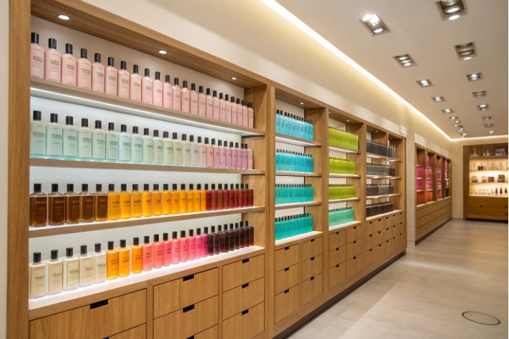 Colorful body care bottles arranged by shade on wooden retail shelving wall