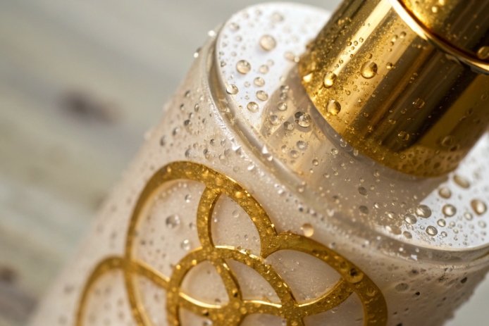 Luxury cosmetic glass bottle with gold cap and water droplets, highlighting decoration finish