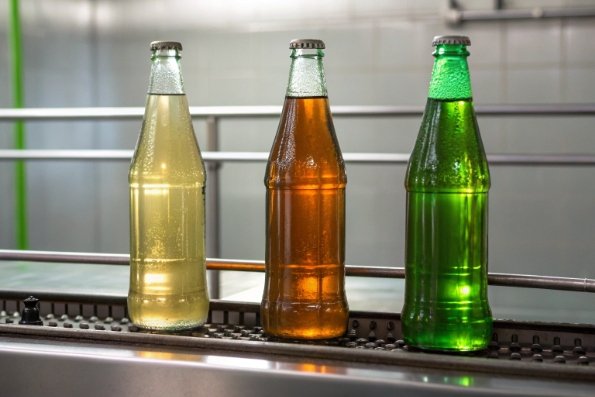 Three filled glass beverage bottles on conveyor line for quality inspection