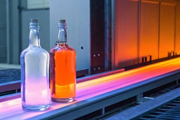Glass liquor bottles on hot forming line with furnace glow in factory
