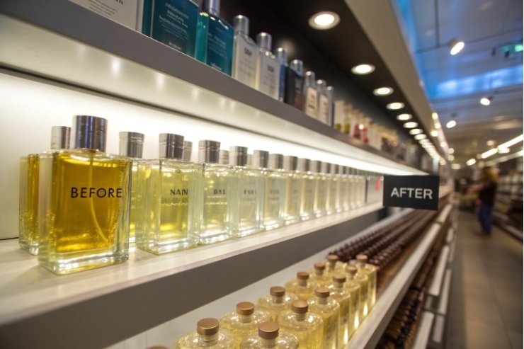 Clear glass perfume tester bottles arranged on illuminated retail shelf with after signage