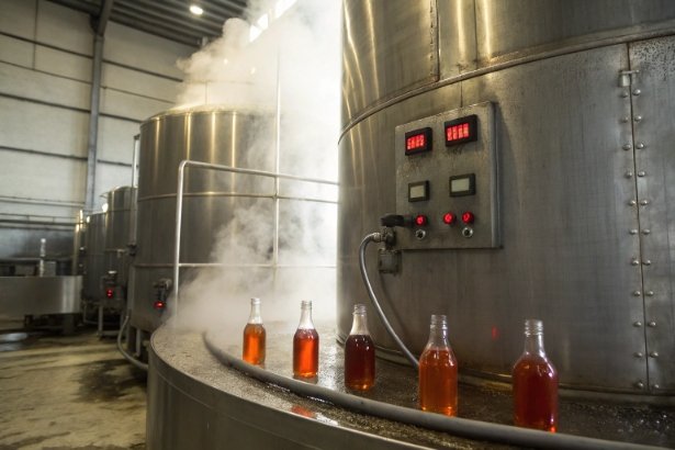 Beverage bottling line with amber liquid bottles beside stainless steel tanks and steam