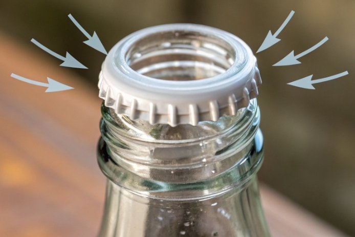 Close-up of bottle finish with cap ring compression arrows showing sealing pressure