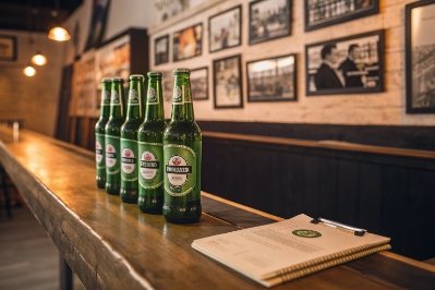 Green beer bottles lined on bar counter with menu notebook in craft brewery taproom