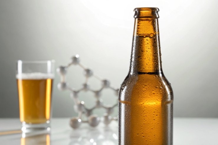 Condensation on amber beer bottle with lager glass and chemistry model background.