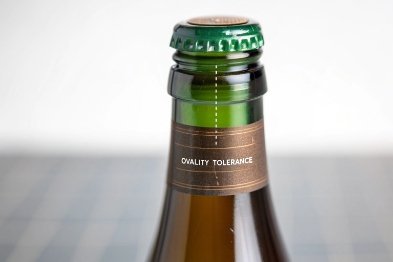 Close-up green beer bottle neck with cap and label reading quality tolerance