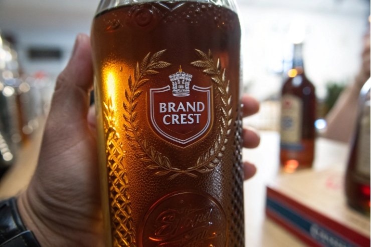Hand holding amber spirits bottle with embossed crest and laurel branding