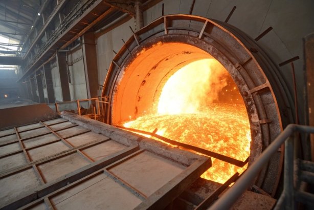 Industrial glass furnace with glowing molten glass pouring inside manufacturing plant