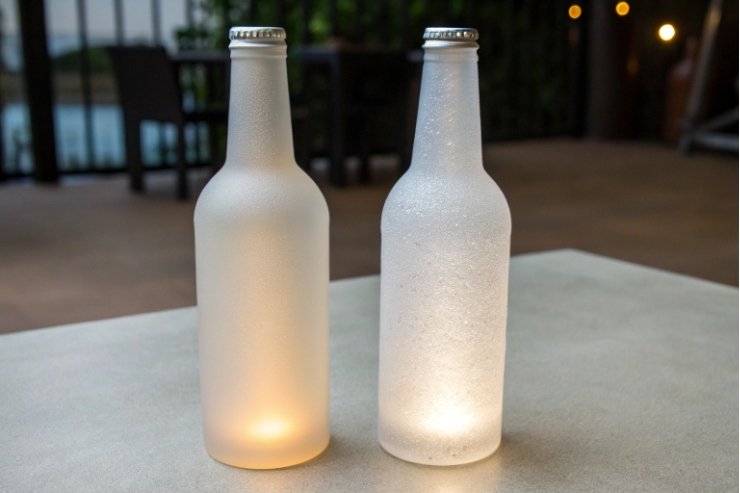 Two illuminated frosted beer bottles glowing softly on outdoor evening table