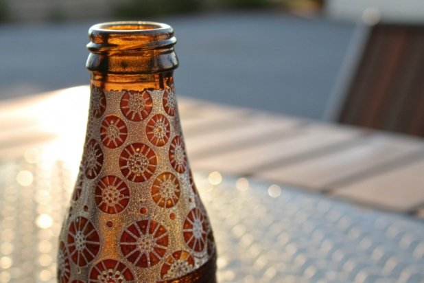 Decorated amber glass bottle neck with textured pattern and warm sunlight bokeh