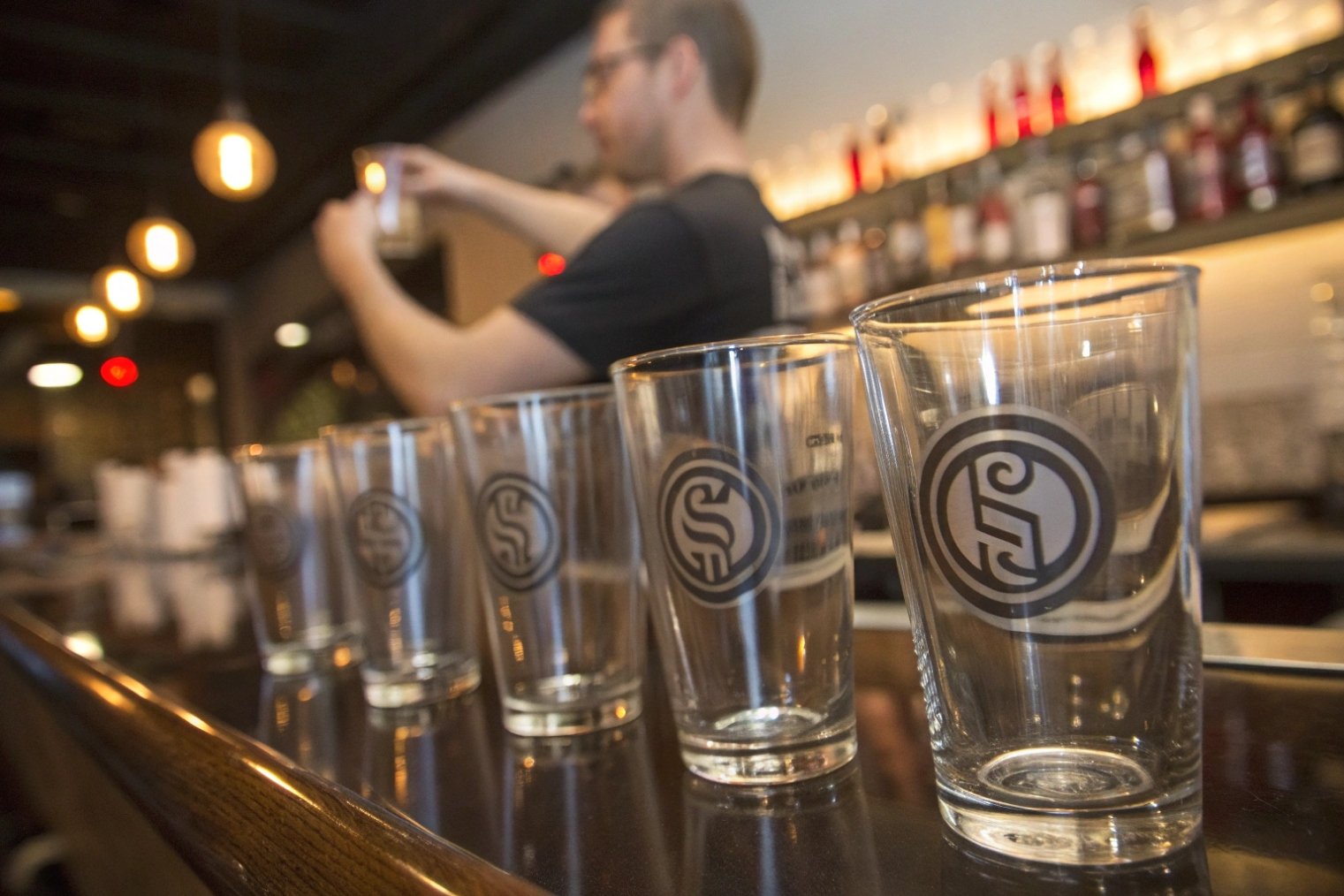 Branded beer glasses lined on bar counter with bartender in background