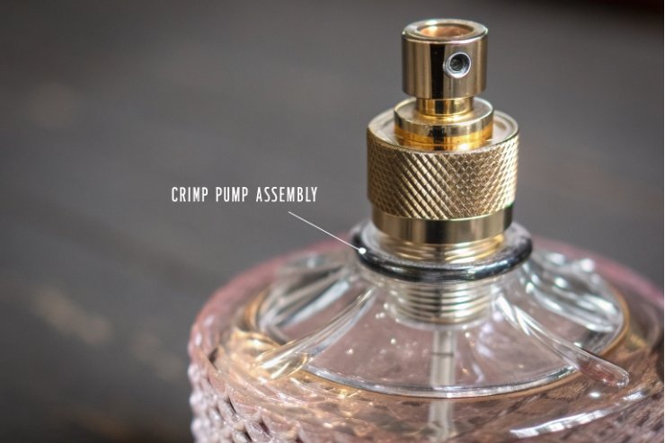 Close up of gold crimp pump assembly on textured glass perfume bottle