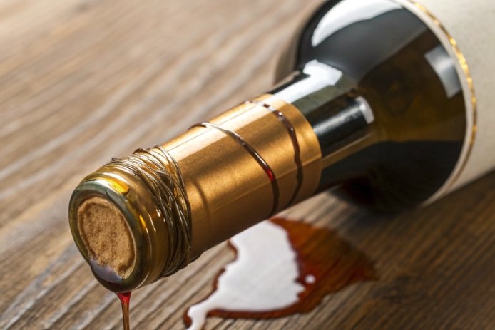 Leaking wine bottle on wooden table showing spill, highlighting closure and seal issues