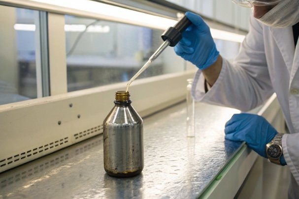 Lab technician pipetting liquid into metal bottle for formulation and stability testing