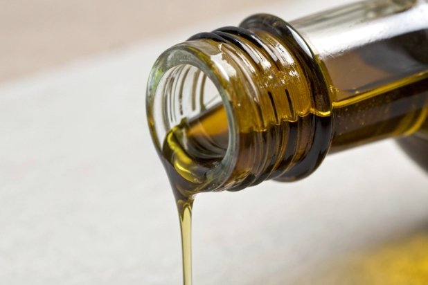 Close-up of olive oil pouring from glass bottle neck showing smooth drip control