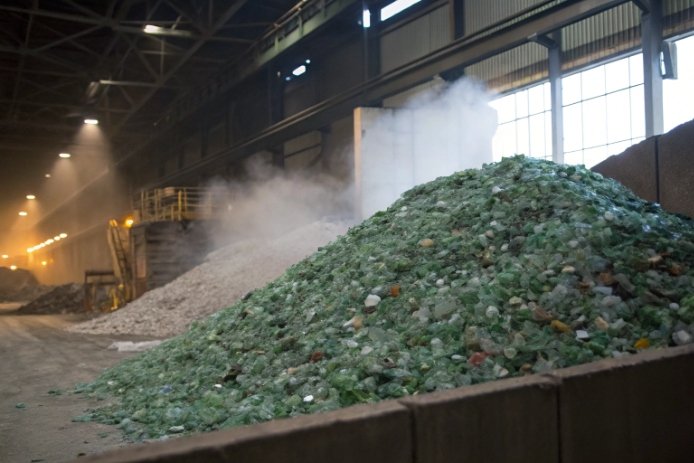 Green recycled glass cullet piles inside industrial recycling facility with dust and steam