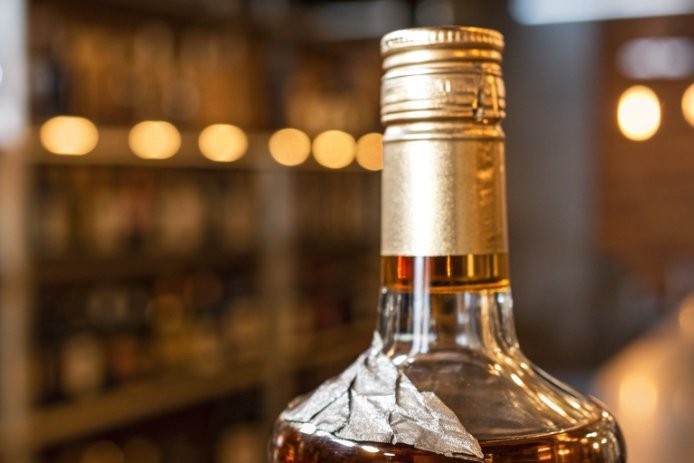 Close-up of liquor glass bottle neck with tamper-evident seal and metal cap