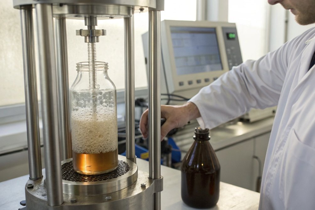 Technician testing carbonated beverage glass bottle resistance under pressure in laboratory equipment