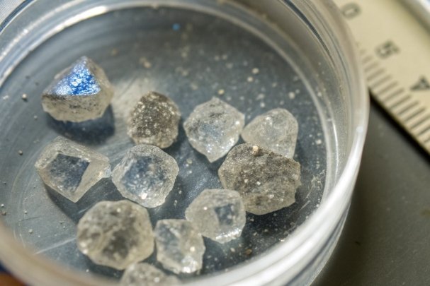Raw mineral crystals in petri dish beside measuring ruler for analysis