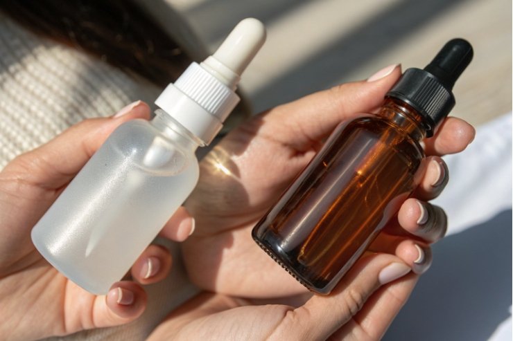 Woman holding frosted and amber glass dropper bottles in natural sunlight