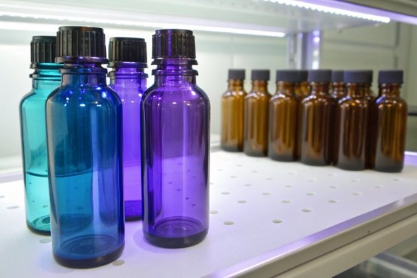 Blue and purple glass bottles with caps on shelf beside amber bottles in lab