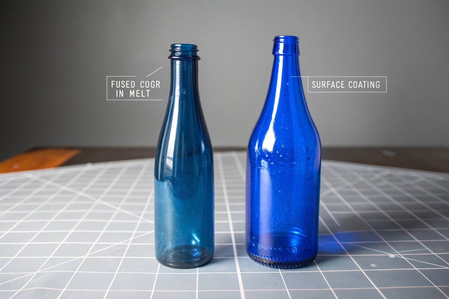 Comparison of fused color and surface coated blue glass beverage bottles on cutting mat.