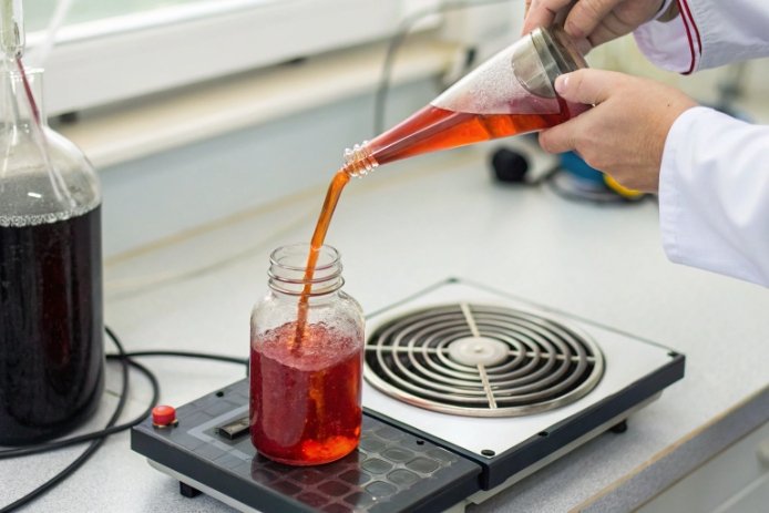 Lab technician pouring hot liquid into jar on heating plate for thermal shock evaluation