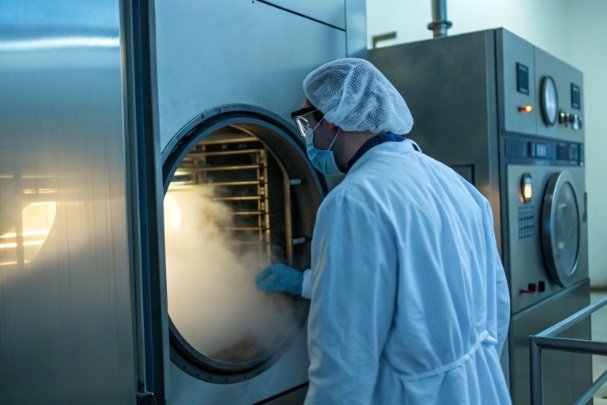 Cleanroom technician opening sterilization autoclave with steam for bottle sanitation