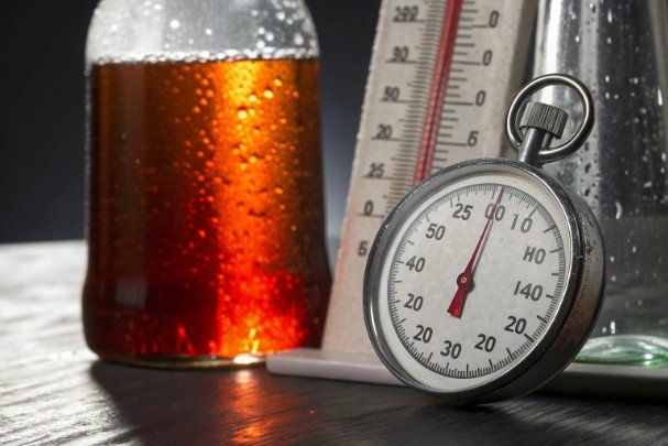 Beverage bottle with amber liquid beside stopwatch and thermometer for quality testing