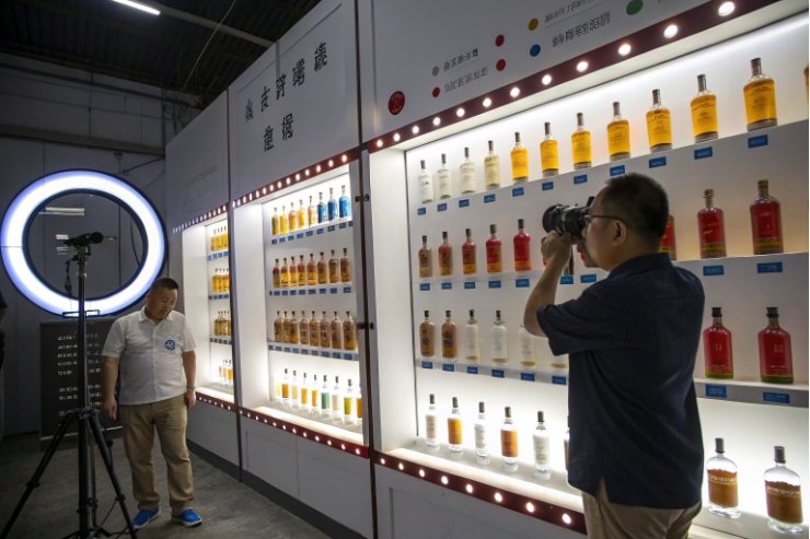 Photographer shooting liquor bottles on illuminated display wall at packaging showroom